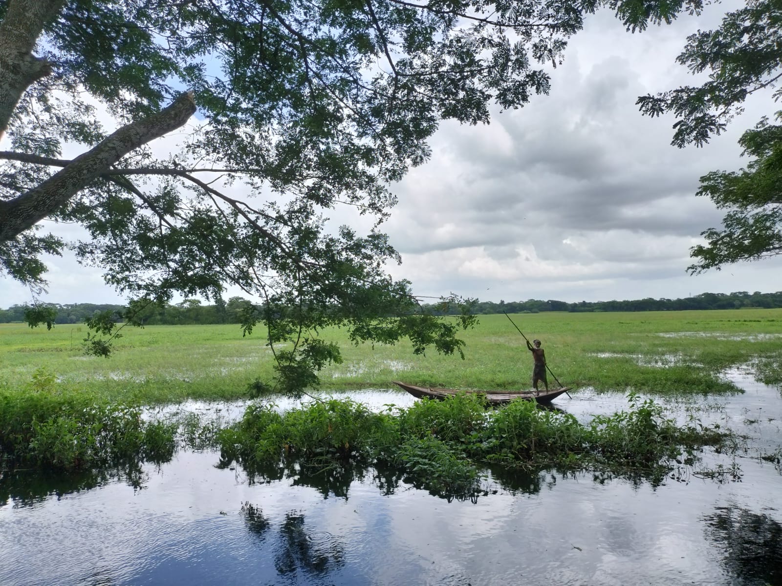 Fisherman poling a wooden boat across a vast green floodplain at ASTANA Resort